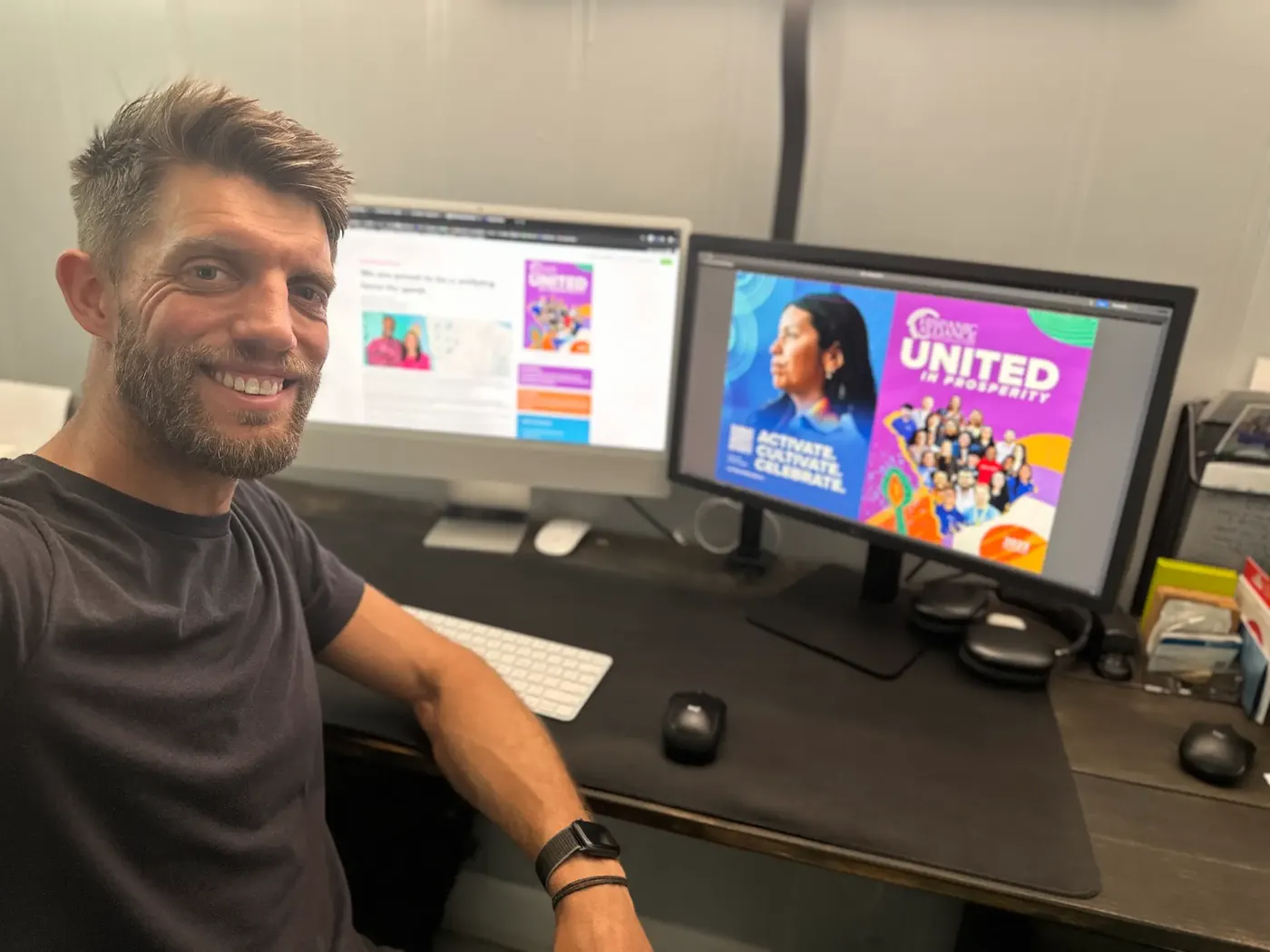 Andrew Skinner smiling at his desk in front of two monitors showing nonprofit website and campaign designs