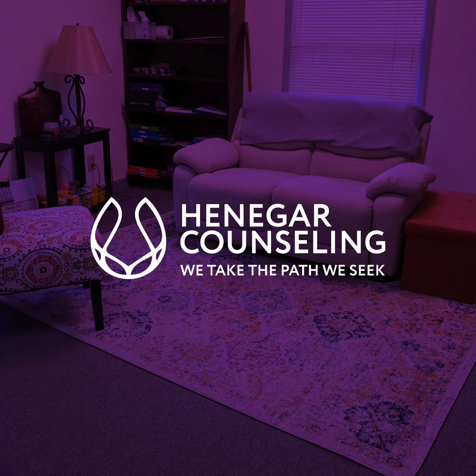 Henegar Counseling logo and tagline We Take the Path We Seek in white over a purple-tinted counseling room with a loveseat and rug