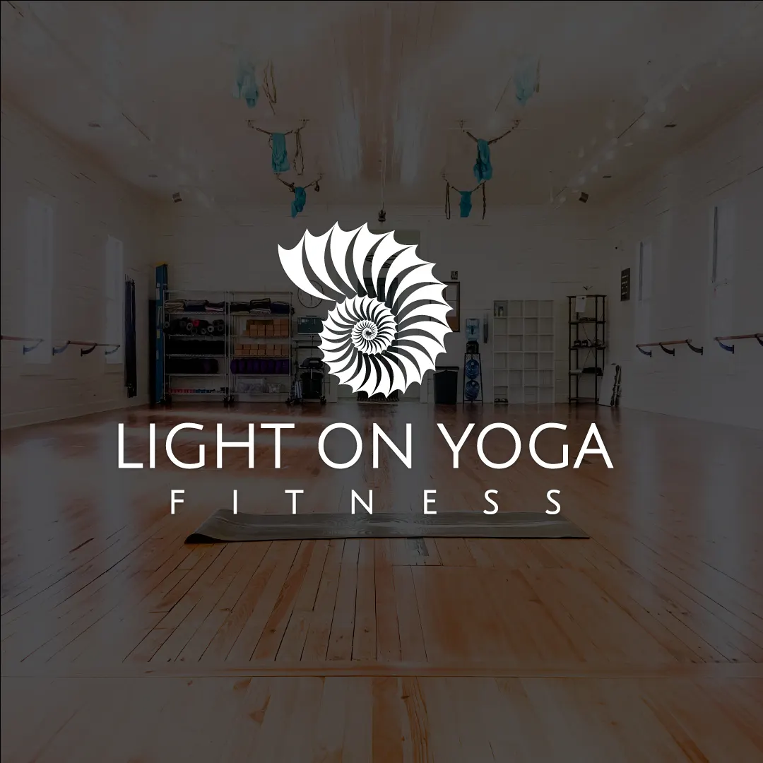 Light on Yoga Fitness nautilus shell logo over a dimmed photo of the studio's wood-floored practice room with a single yoga mat